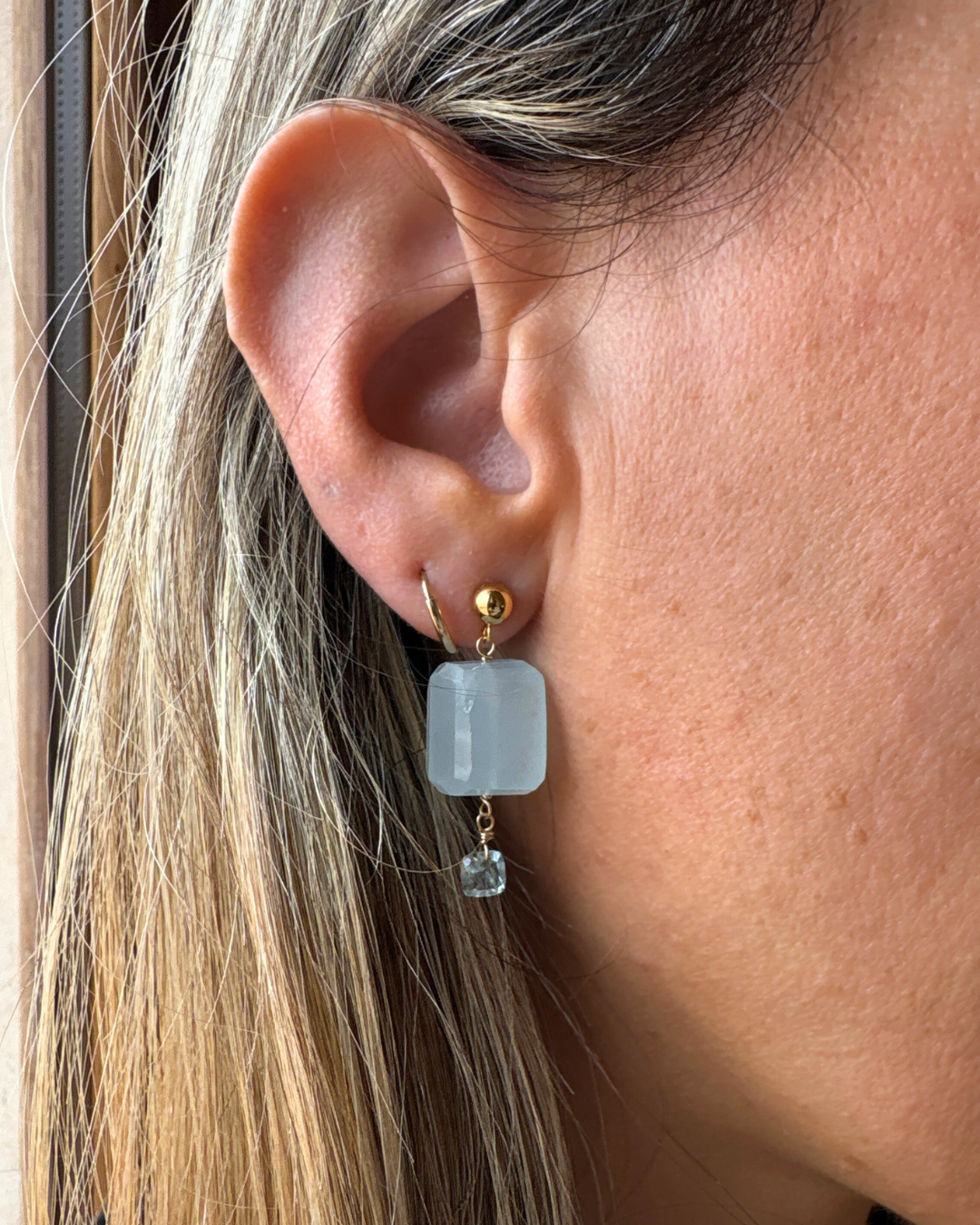 Close-up of an ear wearing a gold earring with a light blue stone.